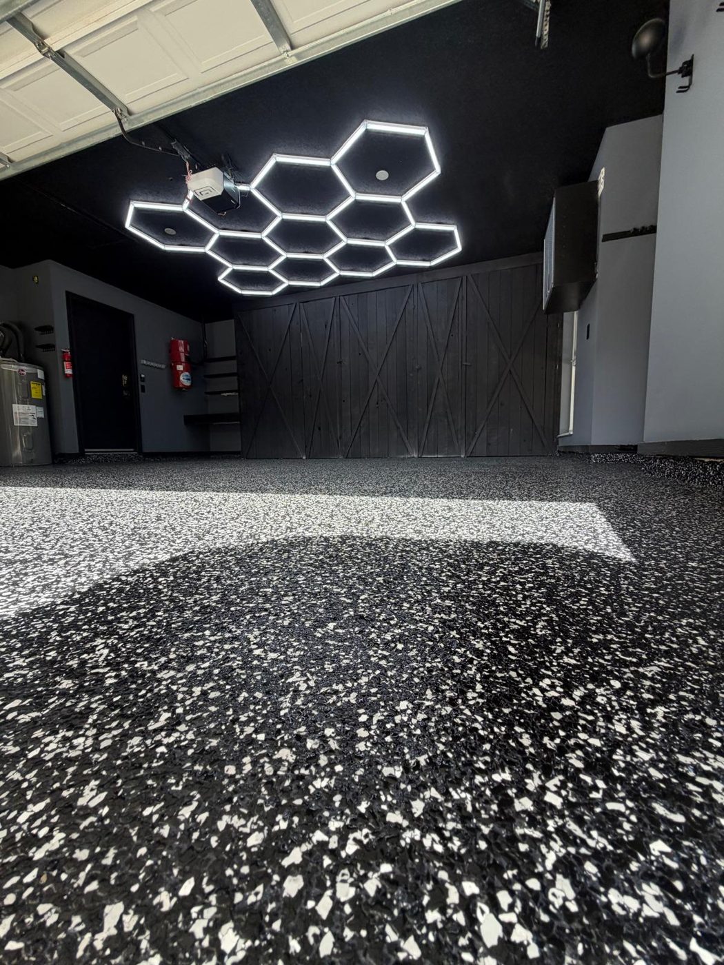 Garage with an illuminated hexagon LED ceiling grid above a black-and-white flake floor